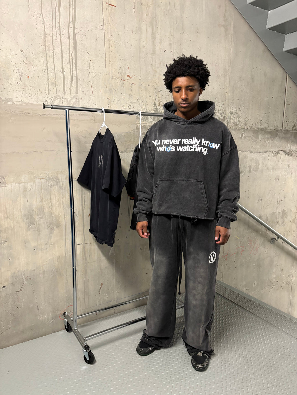 Person wearing a black hoodie with text and dark pants standing on a tiled floor.